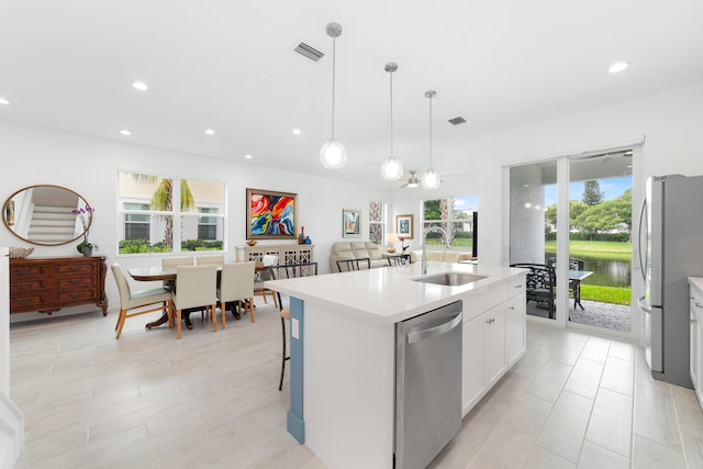 kitchen with appliances with stainless steel finishes, sink, an island with sink, hanging light fixtures, and white cabinetry