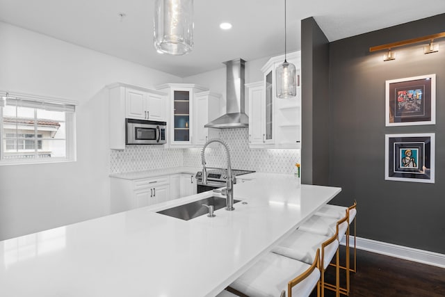 kitchen with decorative backsplash, a breakfast bar, white cabinets, pendant lighting, and wall chimney range hood