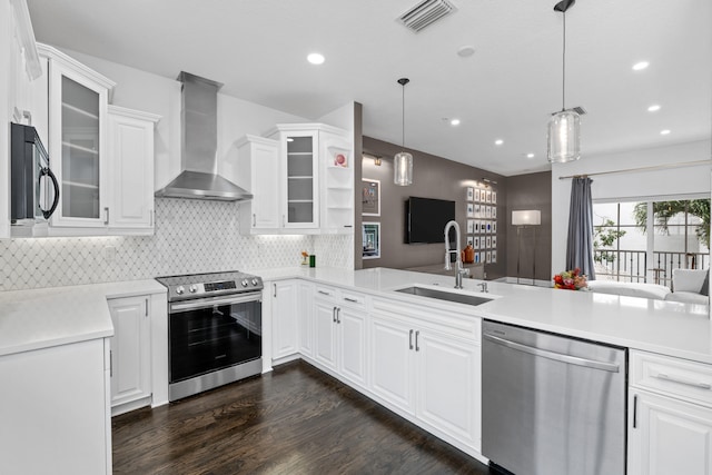 kitchen featuring pendant lighting, white cabinets, sink, wall chimney range hood, and stainless steel appliances