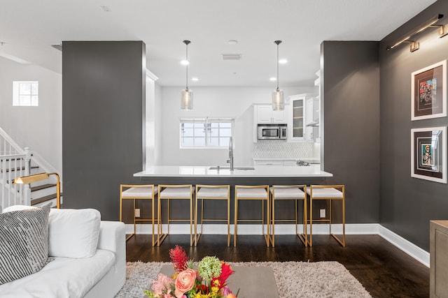 kitchen with dark wood-type flooring, sink, hanging light fixtures, white cabinets, and a kitchen bar