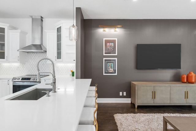 kitchen featuring wall chimney range hood, pendant lighting, dark wood-type flooring, decorative backsplash, and white cabinets