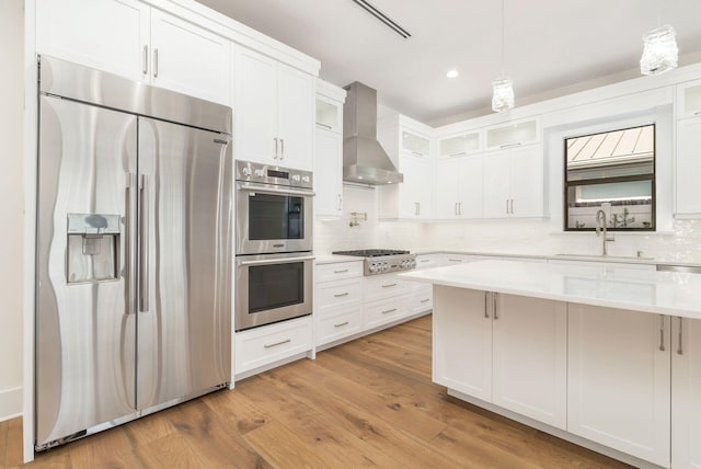 kitchen with wall chimney exhaust hood, light hardwood / wood-style floors, appliances with stainless steel finishes, and sink