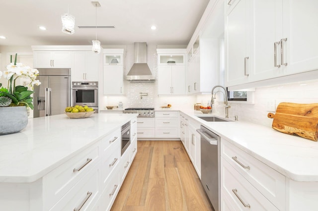 kitchen with sink, white cabinets, hanging light fixtures, built in appliances, and wall chimney range hood