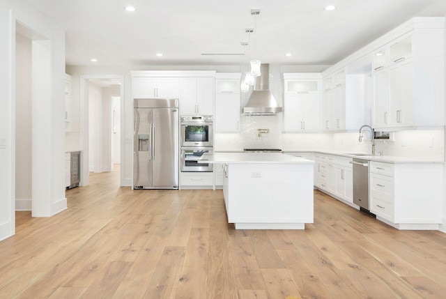 kitchen with a center island, wall chimney range hood, appliances with stainless steel finishes, and light wood-type flooring