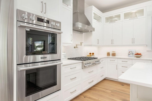 kitchen with white cabinetry, appliances with stainless steel finishes, wall chimney exhaust hood, and light hardwood / wood-style flooring