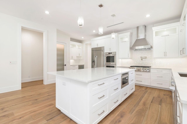 kitchen featuring white cabinets, built in appliances, wall chimney range hood, and a center island