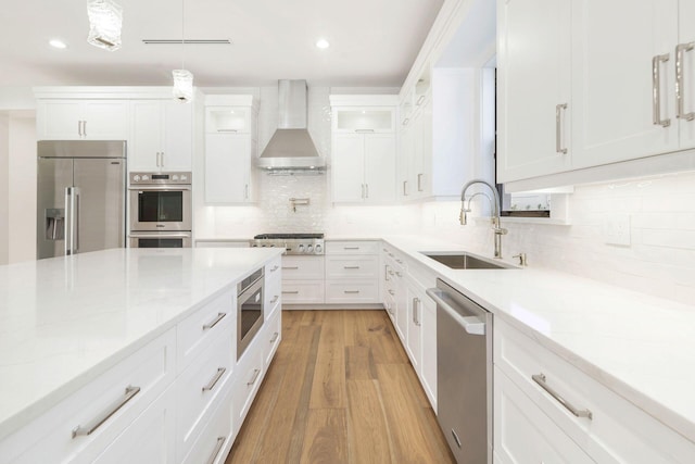 kitchen featuring white cabinets, sink, light hardwood / wood-style floors, wall chimney range hood, and built in appliances