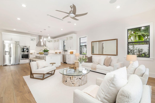 living room featuring ceiling fan, sink, and light wood-type flooring