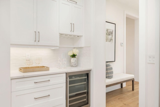 bar featuring wine cooler, tasteful backsplash, white cabinets, and light hardwood / wood-style flooring