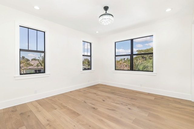 spare room featuring a notable chandelier and light wood-type flooring