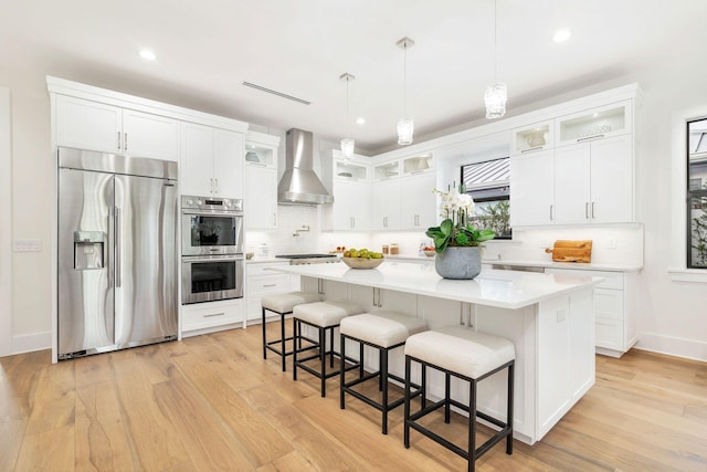 kitchen with stainless steel appliances, a kitchen island, a kitchen breakfast bar, and wall chimney exhaust hood