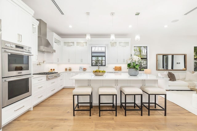 kitchen with white cabinetry, wall chimney exhaust hood, stainless steel appliances, and a center island