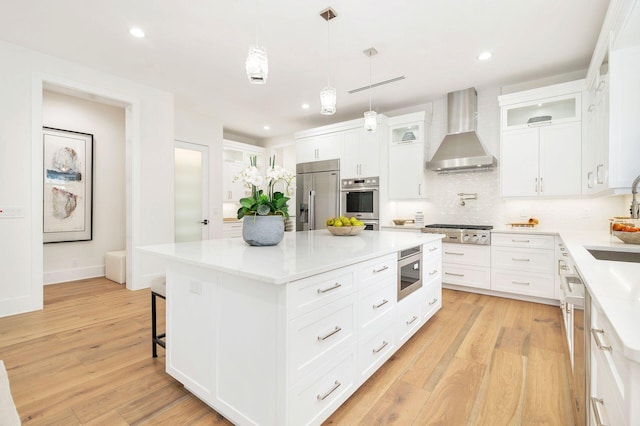 kitchen featuring a center island, built in appliances, white cabinets, and wall chimney exhaust hood