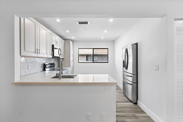 kitchen featuring decorative backsplash, light hardwood / wood-style flooring, stainless steel appliances, kitchen peninsula, and white cabinetry