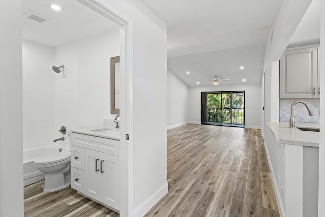 interior space featuring ceiling fan, vanity, tiled shower / bath combo, wood-type flooring, and toilet