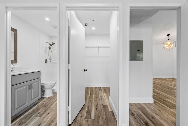 bathroom featuring vanity, electric panel, a tile shower, hardwood / wood-style flooring, and toilet