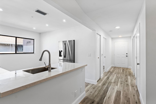 kitchen featuring light stone counters, sink, light hardwood / wood-style floors, and stainless steel refrigerator with ice dispenser