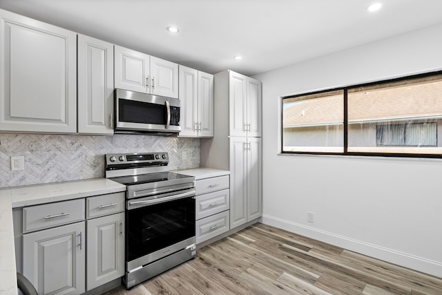 kitchen with tasteful backsplash, appliances with stainless steel finishes, light hardwood / wood-style flooring, and light stone counters