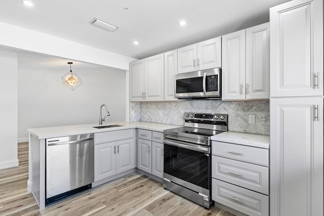 kitchen with stainless steel appliances, sink, kitchen peninsula, light hardwood / wood-style flooring, and decorative light fixtures