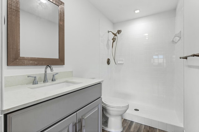 bathroom featuring a tile shower, hardwood / wood-style floors, vanity, and toilet