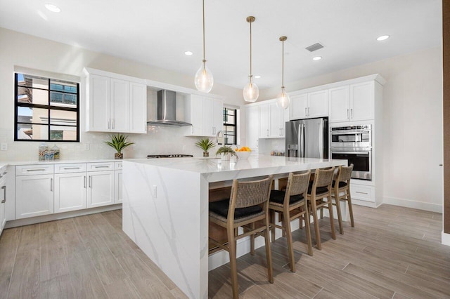 kitchen featuring wall chimney exhaust hood, a center island, stainless steel appliances, and white cabinets