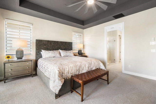 bedroom featuring light carpet, ensuite bath, a raised ceiling, and ceiling fan