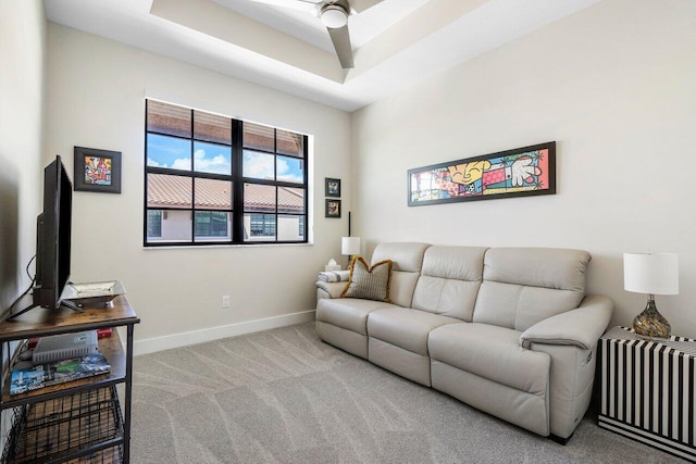 carpeted living room with a raised ceiling and ceiling fan