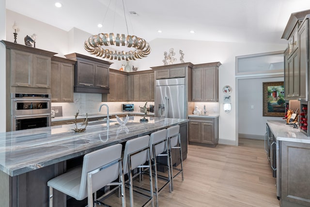 kitchen featuring appliances with stainless steel finishes, a large island, lofted ceiling, pendant lighting, and light hardwood / wood-style flooring