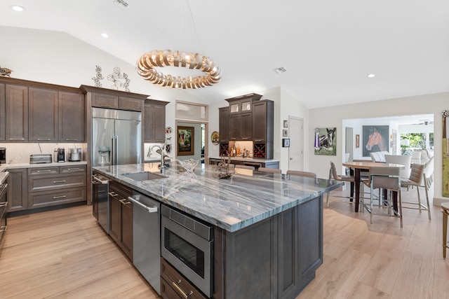 kitchen with a spacious island, built in appliances, sink, vaulted ceiling, and light hardwood / wood-style floors