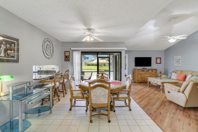 dining room featuring vaulted ceiling, a textured ceiling, light wood-type flooring, and ceiling fan