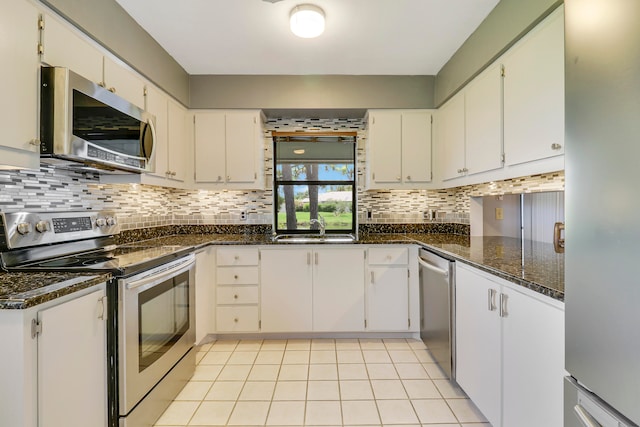 kitchen featuring appliances with stainless steel finishes, white cabinets, dark stone countertops, and sink