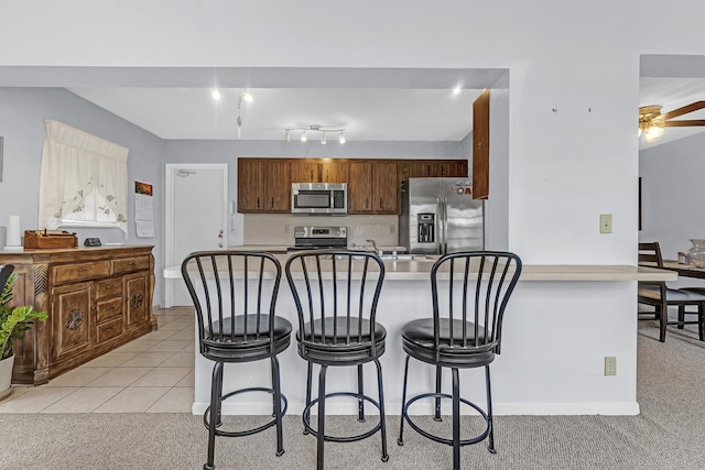 kitchen featuring light tile patterned flooring, ceiling fan, stainless steel appliances, and a kitchen breakfast bar