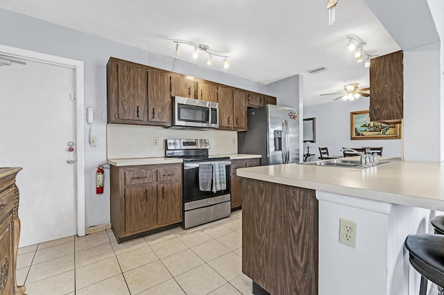 kitchen with light tile patterned floors, kitchen peninsula, stainless steel appliances, a kitchen breakfast bar, and sink