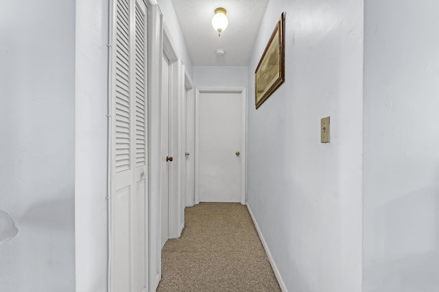 hall with light colored carpet and a textured ceiling