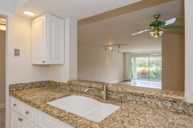 kitchen featuring light stone countertops, white cabinets, sink, and ceiling fan