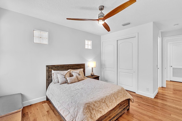 bedroom with a closet, a textured ceiling, light wood-type flooring, and ceiling fan