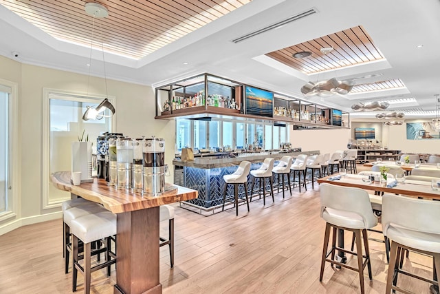 dining space featuring light hardwood / wood-style flooring, ornamental molding, indoor bar, and a tray ceiling