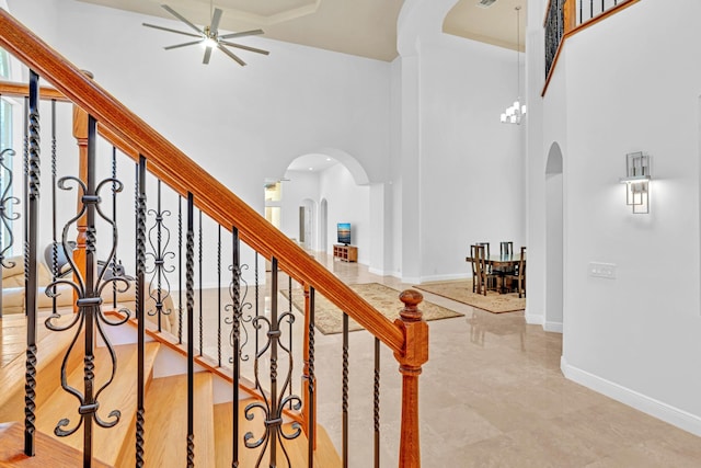 staircase featuring ceiling fan with notable chandelier, wood-type flooring, and a towering ceiling