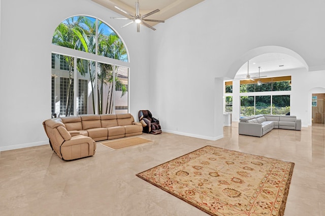 living room featuring ceiling fan, a healthy amount of sunlight, and a towering ceiling