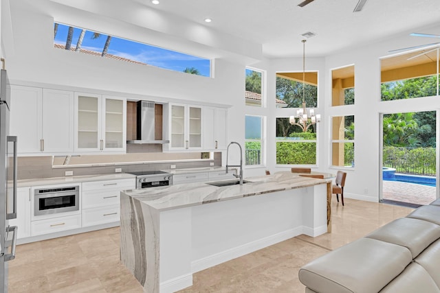 kitchen featuring white cabinets, an island with sink, appliances with stainless steel finishes, wall chimney exhaust hood, and sink