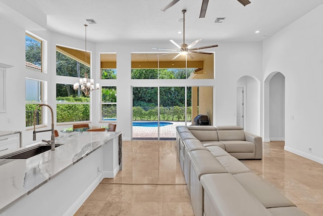 living room with sink, a high ceiling, a textured ceiling, and ceiling fan with notable chandelier