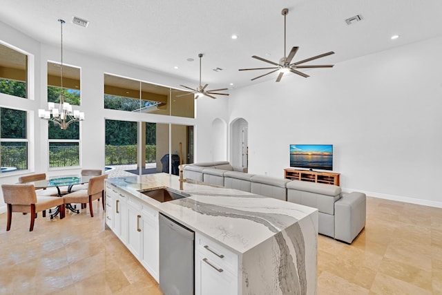 kitchen with a high ceiling, an island with sink, stainless steel dishwasher, white cabinets, and light stone counters