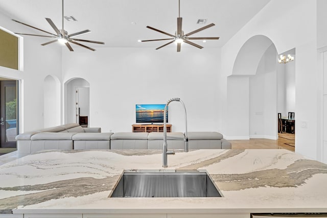 kitchen with light stone countertops, ceiling fan, a towering ceiling, and sink