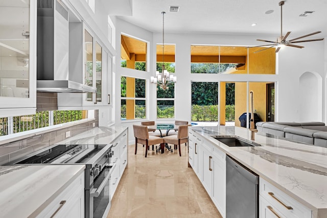 kitchen featuring wall chimney range hood, stainless steel appliances, white cabinets, light stone counters, and decorative backsplash