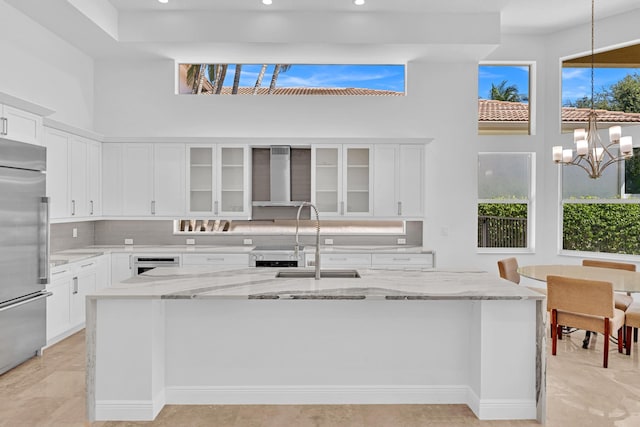 kitchen with wall chimney exhaust hood, built in refrigerator, sink, and white cabinets