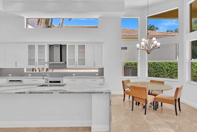 kitchen featuring wall chimney range hood, a wealth of natural light, and white cabinets