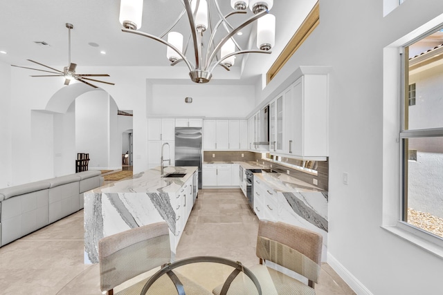 kitchen featuring decorative backsplash, white cabinets, sink, a high ceiling, and light stone counters