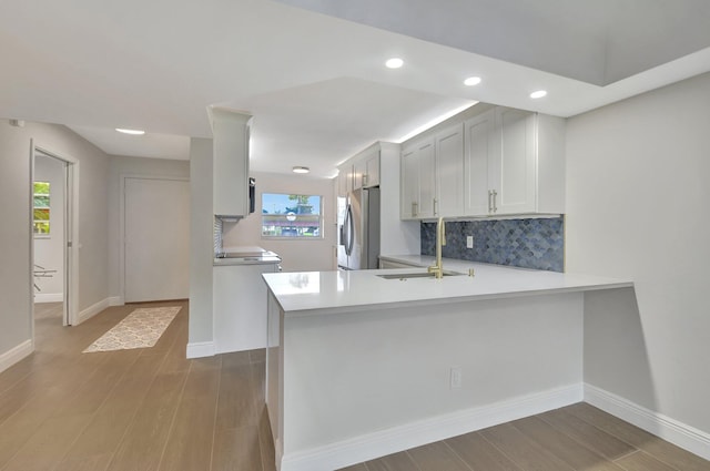 kitchen with light hardwood / wood-style flooring, kitchen peninsula, stainless steel refrigerator with ice dispenser, and white cabinetry