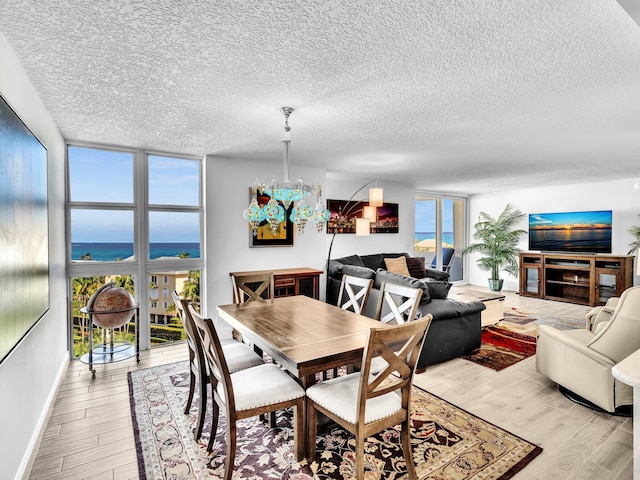 dining area featuring light wood-type flooring, a textured ceiling, a water view, and expansive windows