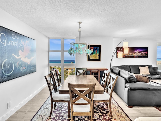 dining room featuring a textured ceiling, a notable chandelier, a wall of windows, a water view, and light hardwood / wood-style flooring